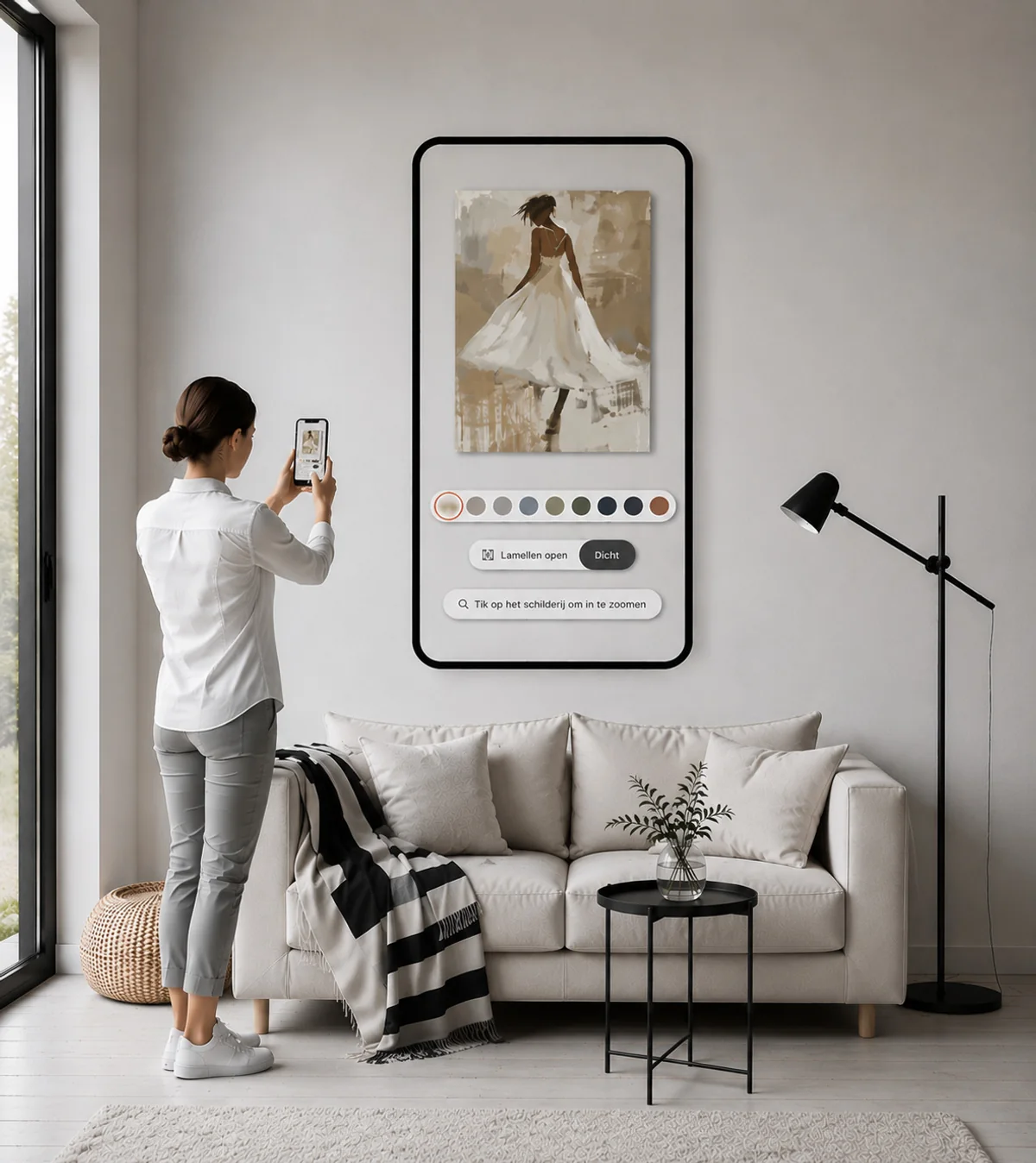 Vrouw richt haar telefoon op de muur boven de bank; op het scherm hangt het schilderij er, met de muurkleuren eronder
